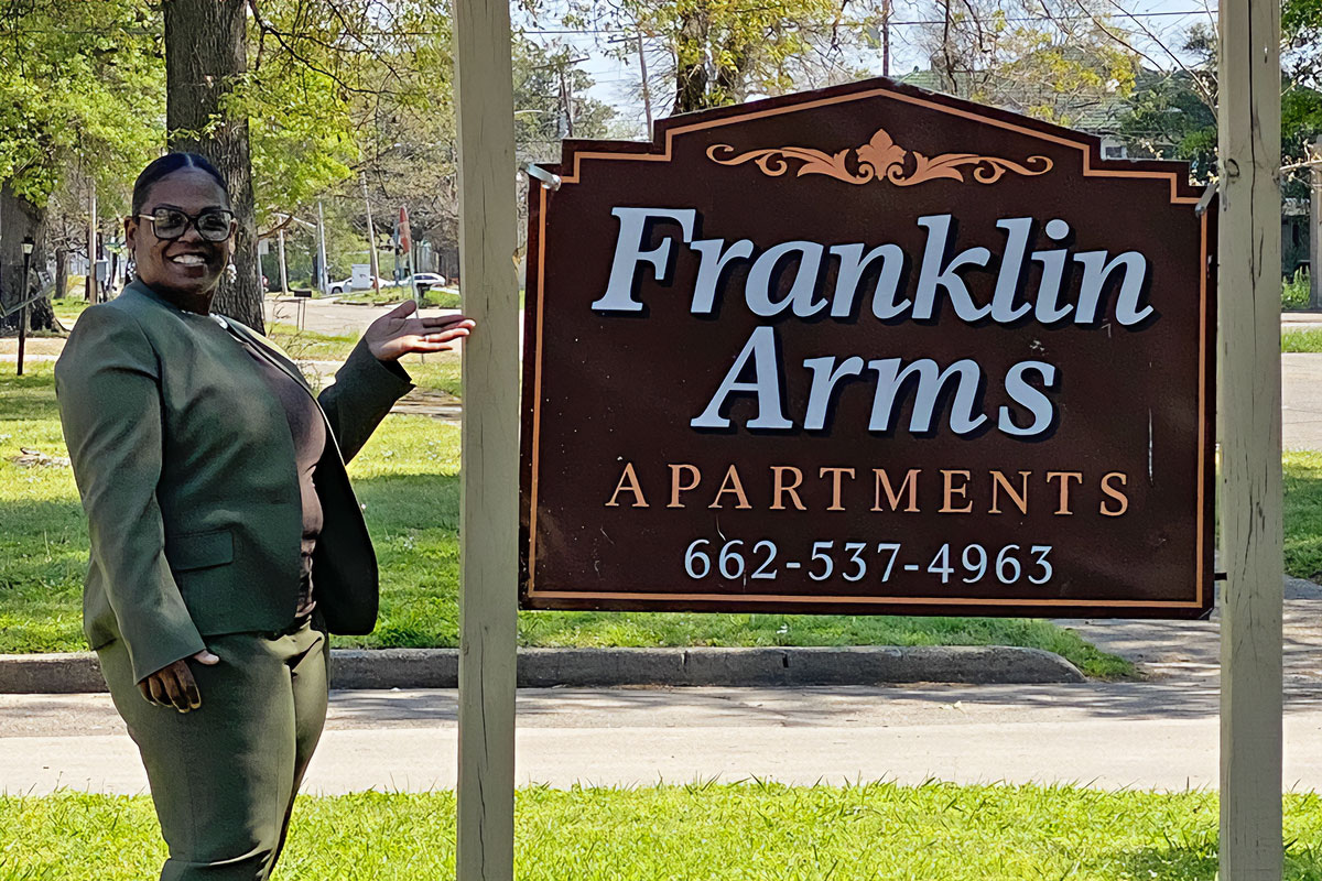 Tonya Franklin stands next to the sign for Franklin Arms Apartments