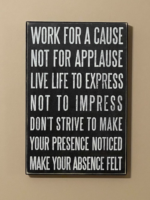 Picture hanging on the wall that reads, "WORK FOR A CAUSE NOT FOR APPLAUSE LIVE LIFE TO EXPRESS NOT TO IMPRESS DON'T STRIVE TO MAKE YOUR PRESENCE NOTICED MAKE YOUR ABSENCE FELT. (life lessons)