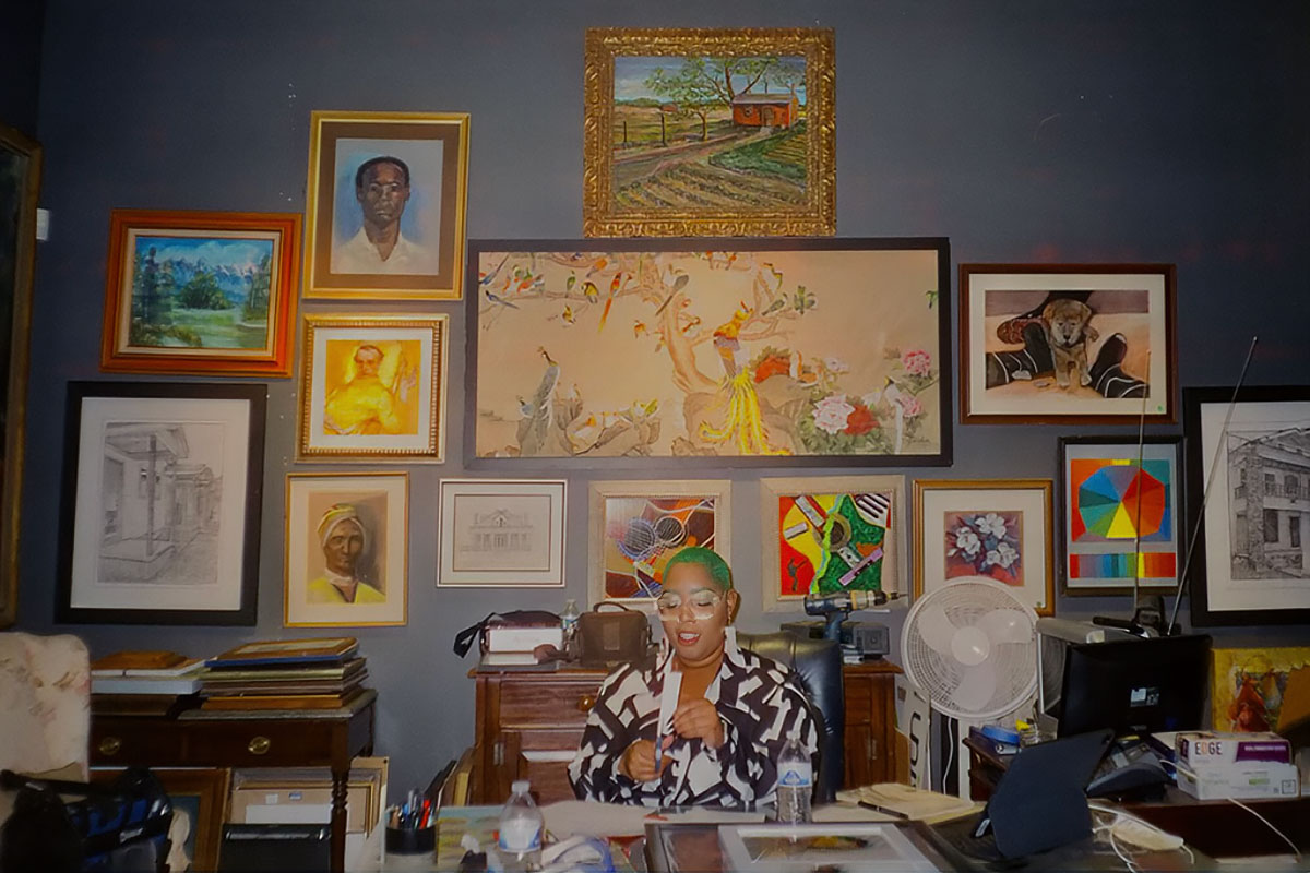 Jasmine Williams sitting in her office, many pieces of framed art hanging behind her