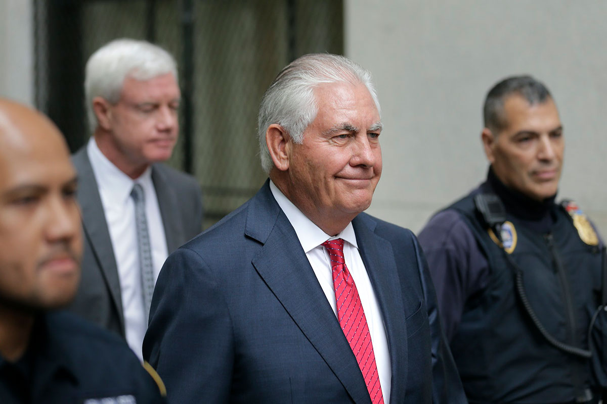 Rex Tillerson, a smiling older man in a suit and tie, walks out of a courthouse with security guards (climate change)