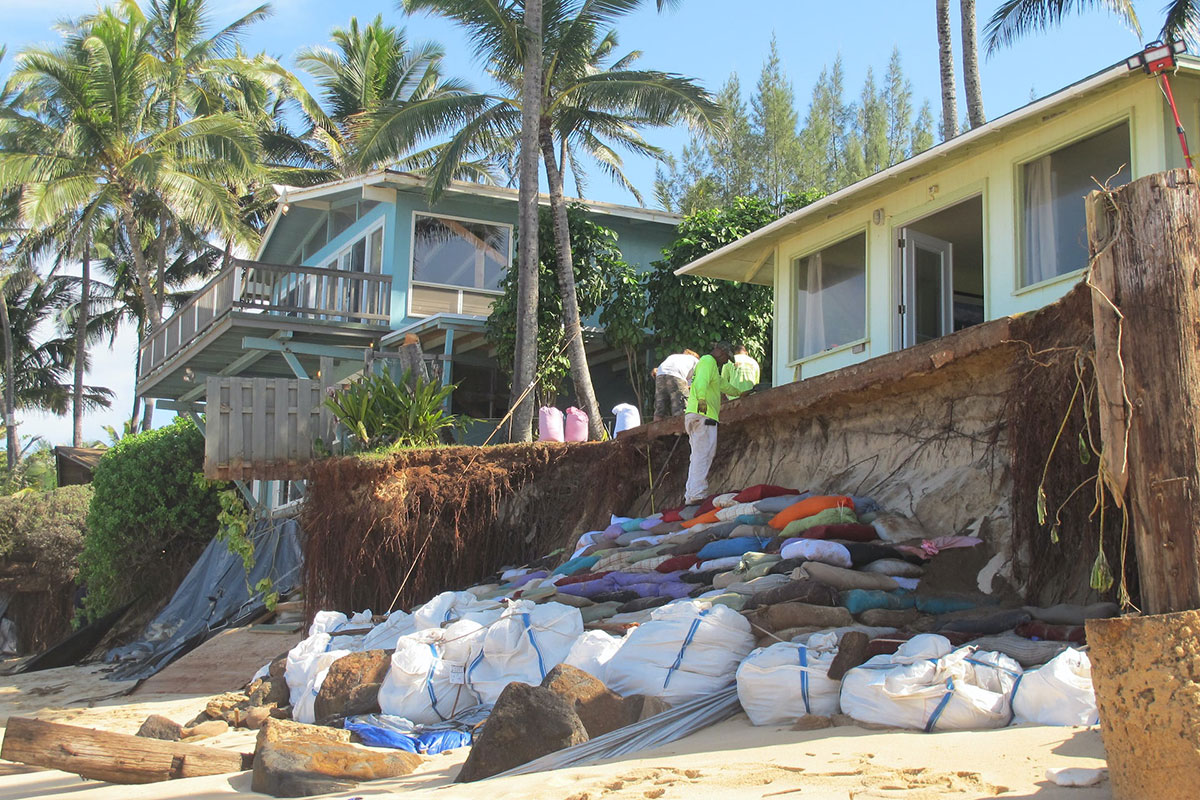 andbags sit outside a home near a beach in Oahu, Hawaii, where waves have eaten into the shoreline almost up to the house (climate change)