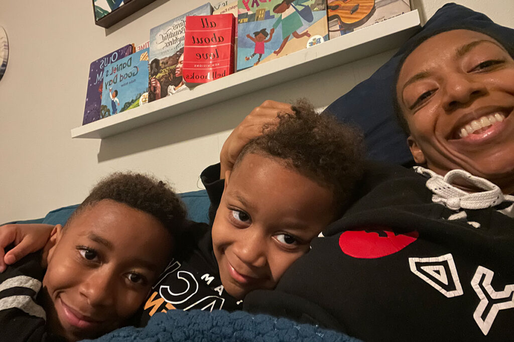 Shanina Carmichael lounges on a couch with her two kids, books on the shelf above them