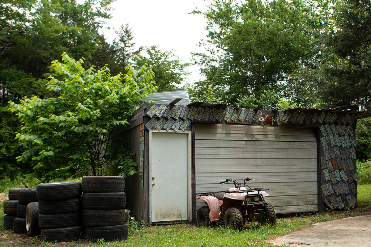 An external view of a storage shed covered decoratively in license plates, stacks of car tires to the left