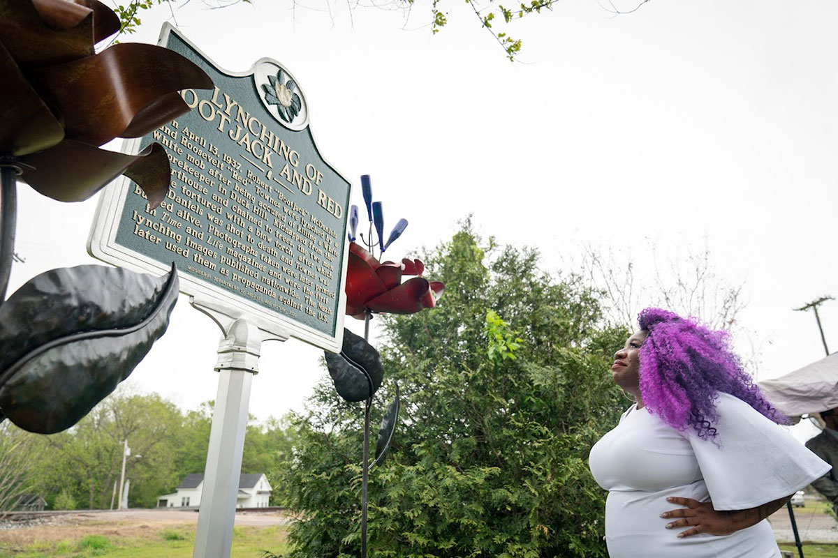 A woman reads a sign with the title Lynching of Bootjack and Red