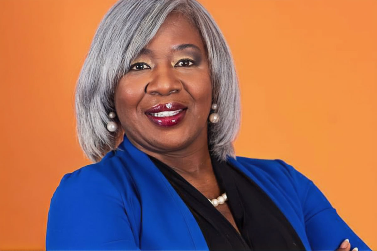 Christiane Williams in a blue and black top standing against an orange background