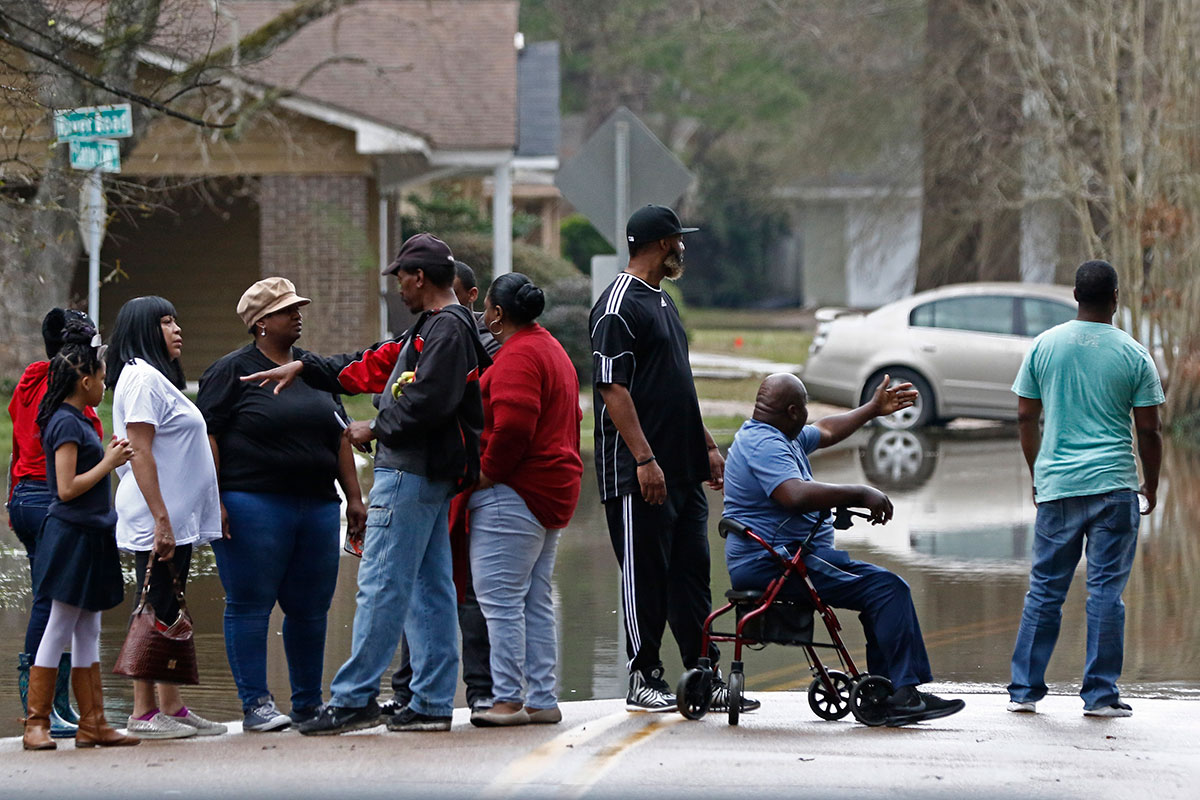 A row of people stand at the end of floodwaters in a neighborhood road