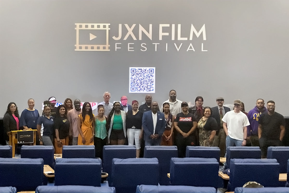 A long line of people posed for a photo in front of a projection of the JXN Film Festival logo and QR Code