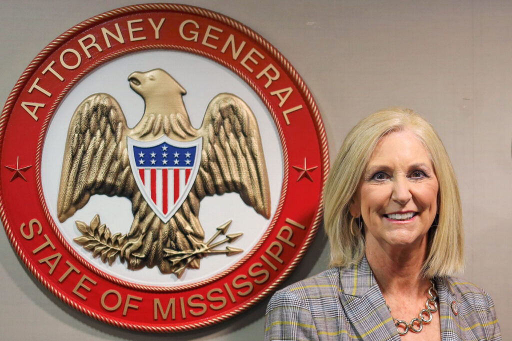 Attorney General Lynn Fitch standing beside the large red State of Mississippi Attorney General seal on a wall