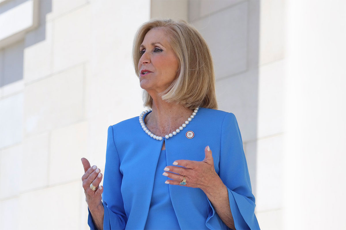 Attorney General Lynn Fitch speaking outside of a white building. She's wearing a blue suit set.