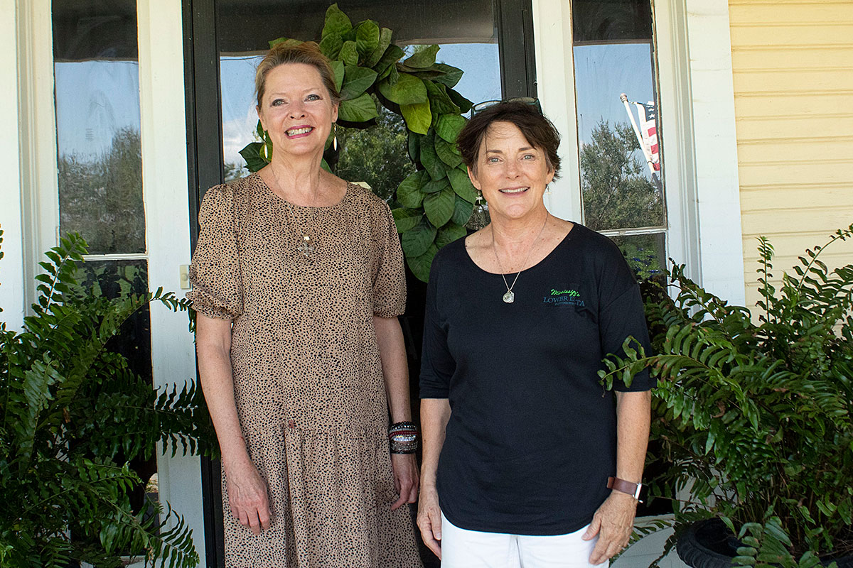 Melissa Thomas (left) and Meg Cooper pose outside of a glass doorway with plants on the sides