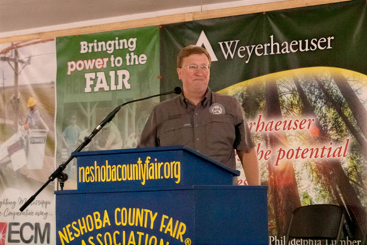 Tate Reeves speaks at a blue podium labeled Neshoba County Fair
