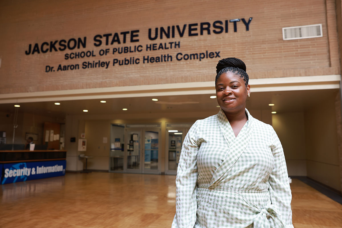 Whitney Perkins in a green and white checkered outfit stands in a lobby outside the JSU School of Public Health