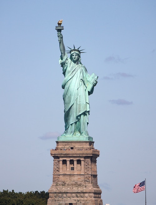 front-facing statue of liberty with an American flag in the right bottom corner (freedom)