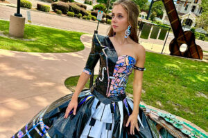 A teen in a dress made of duct tape, mostly black and white with holographic highlights, in a musical theme.