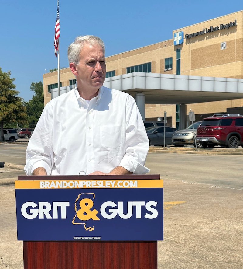 a photo of Brandon Presley standing at a podium that says "BRANDONPRESLEY.COM GRIT & GUTS" in front of the Greenwood Leflore Hospital