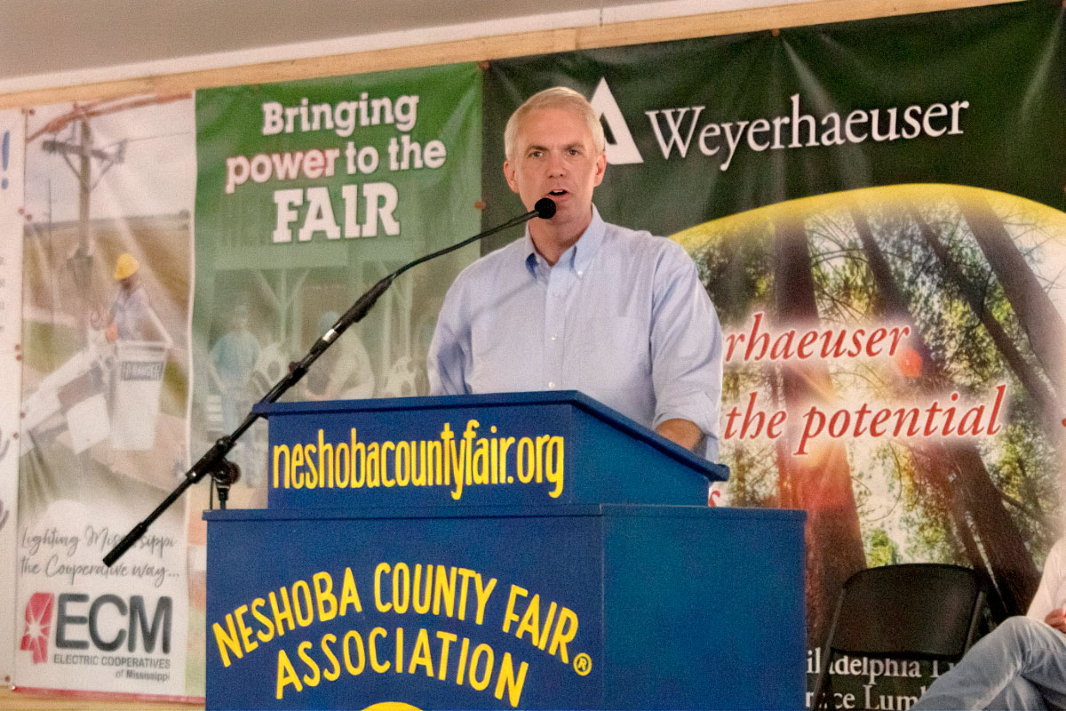 Brandon Presley speaks at a blue podium labeled Neshoba County Fair