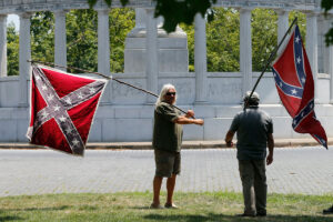 Two men talk while holding confederate flags outside of a monument
