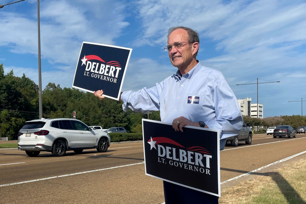 A man holding signs that read "Delbert Lt Governor" by the road side