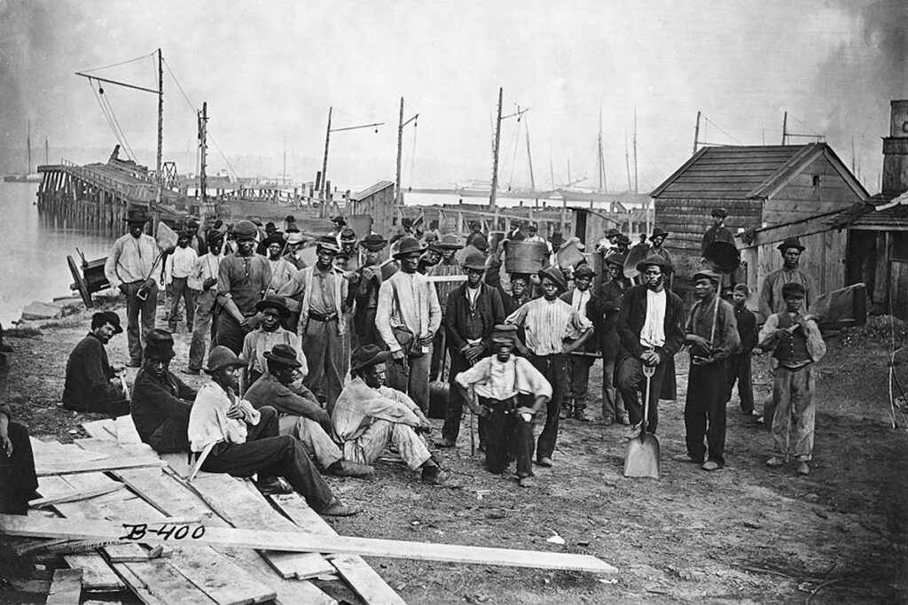 A group of enslaved men stands outside in a shipyard (Enslaved Africans)
