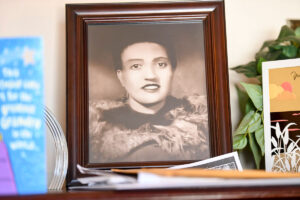 A framed photo of a woman in sepia tone sits on a cluttered mantle