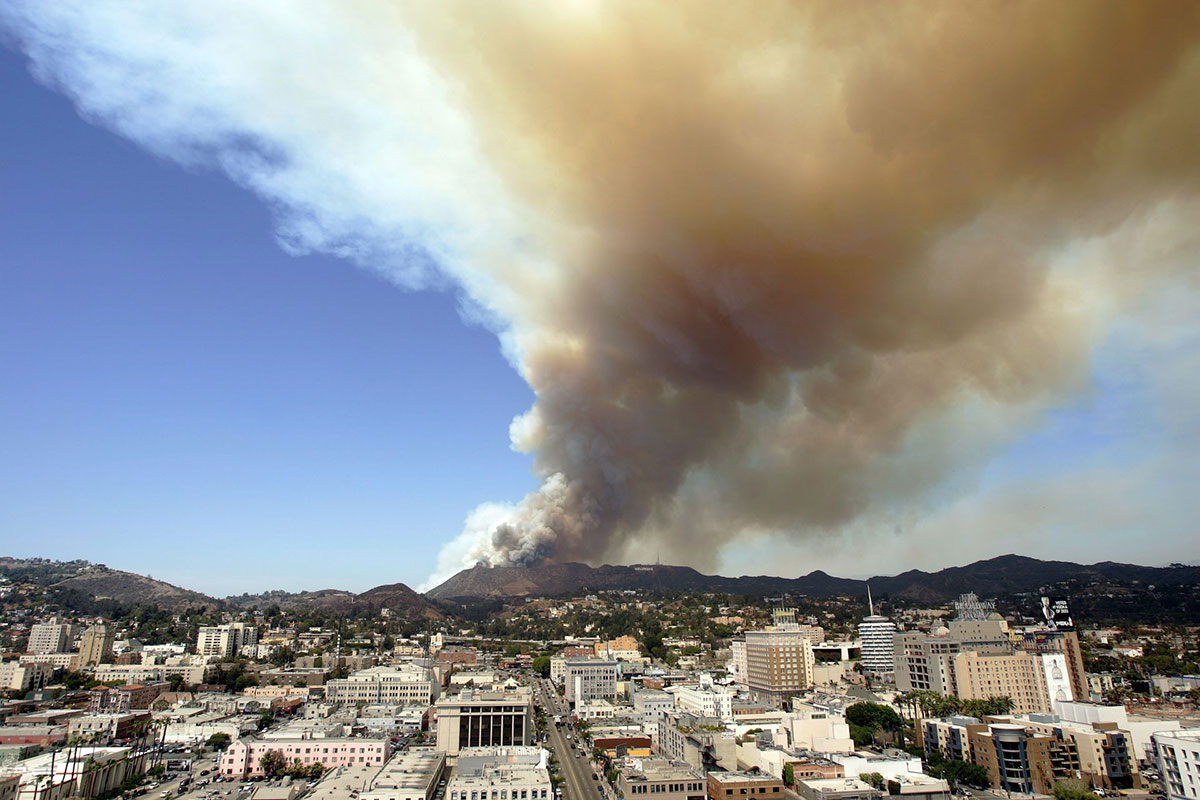 A view across the city shows a column of smoke rising ominously in the hills nearby