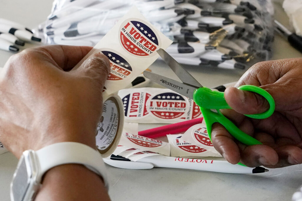 A pair of hands can be seen cutting out the "I Voted in Hinds County" stickers to present the voters at the polling precinct