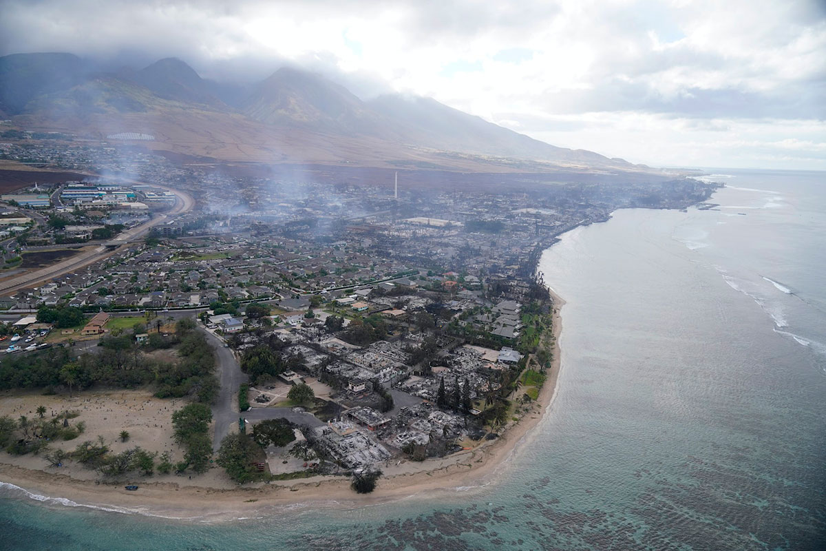 An aerial view of the town of Lahaina, smoke still lingering over the town and obscuring the mountain in the background