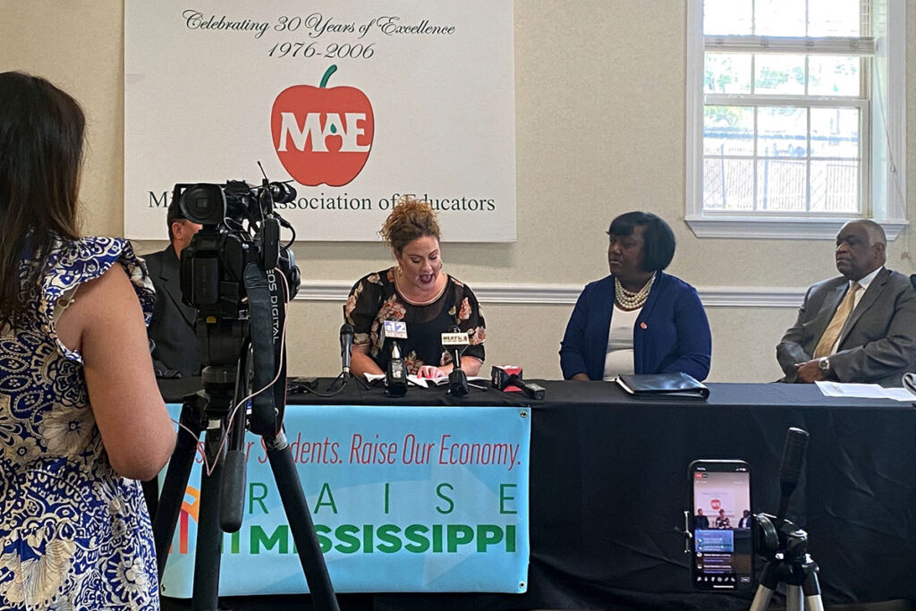 Members of the Mississippi Association of Educators discussing things at a table in front of the press