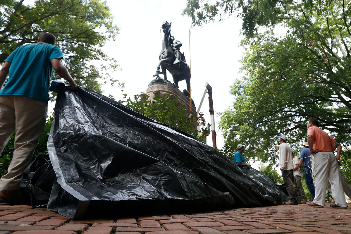 People hold a large tarpaulin beneath a statue of a man riding a horse.