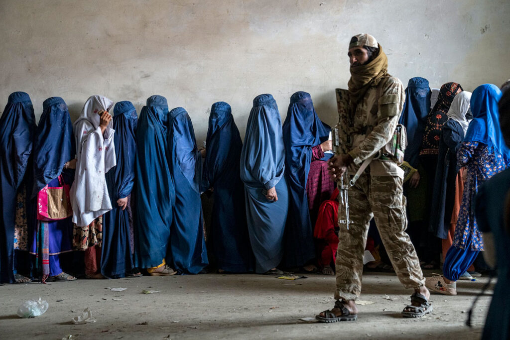 An armed Taliban soldier walks past a line of women (Afghan women)