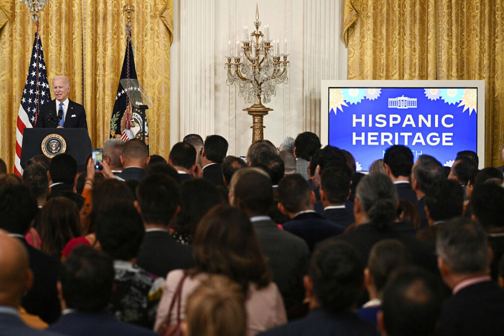 President Biden speaks before a crown in a gold-curtained room for Hispanic Heritage Month