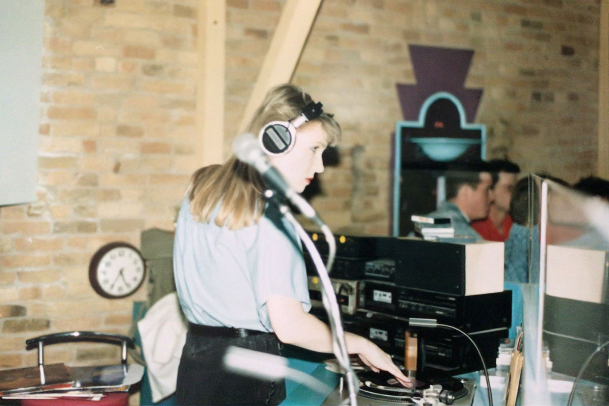 Donna Ladd works behind a table of DJ equipment in a room that's enclosed with brown bricks