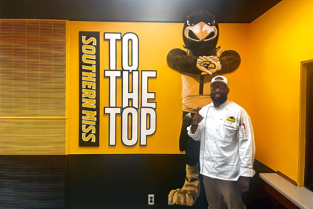 Joshua Cathey, in a chef's coat, stands in front of Southern Miss's Seymore the Eagle