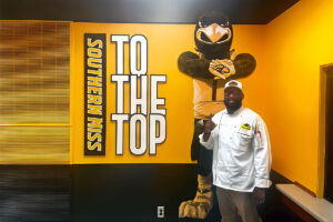 Joshua Cathey, in a chef's coat, stands in front of Southern Miss's Seymore the Eagle