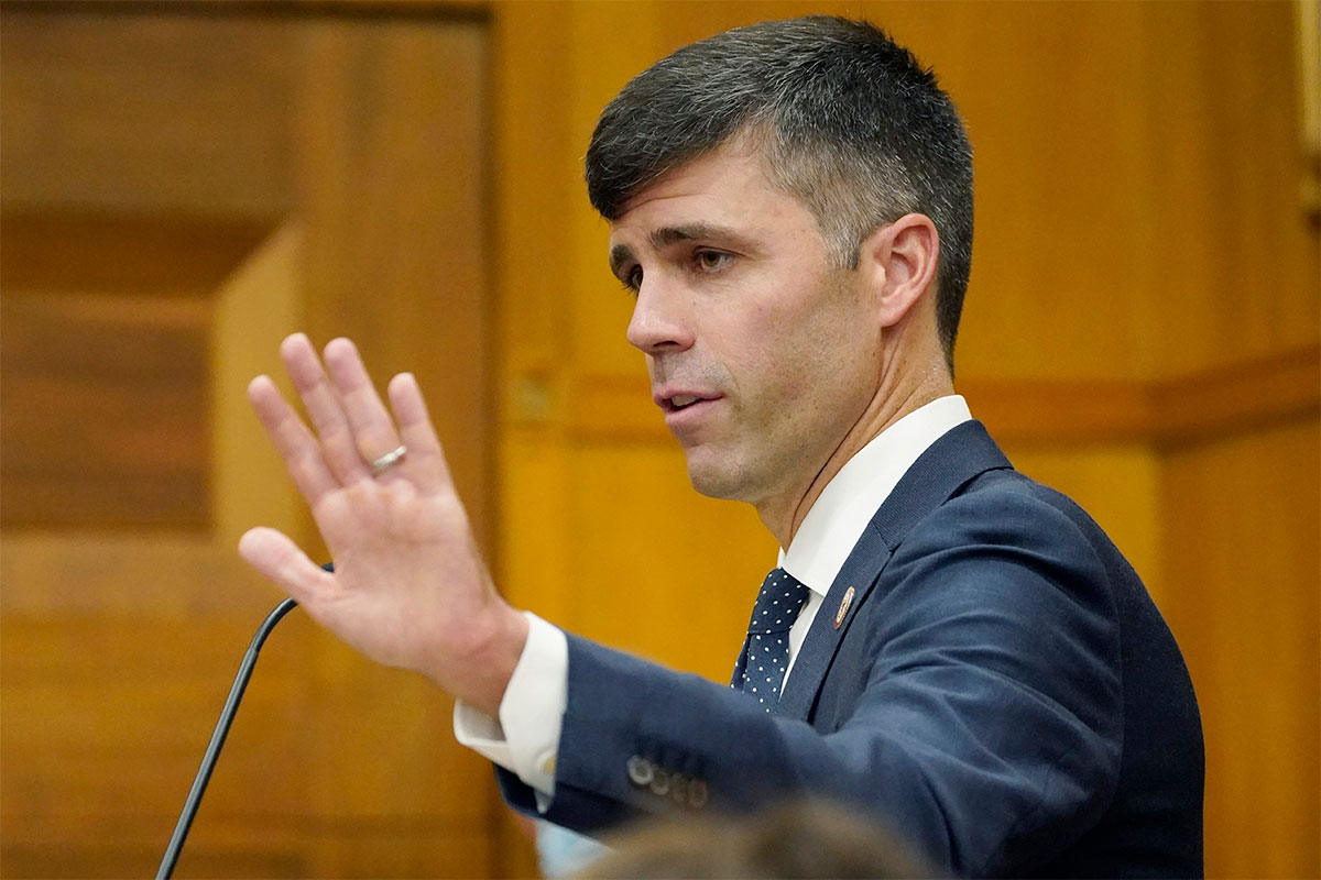 A man in a dark suit holds his hand up while speaking at a podium
