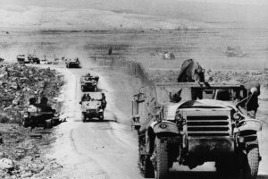 Black and white photo of military vehicles driving down a dry dirt road in Israel