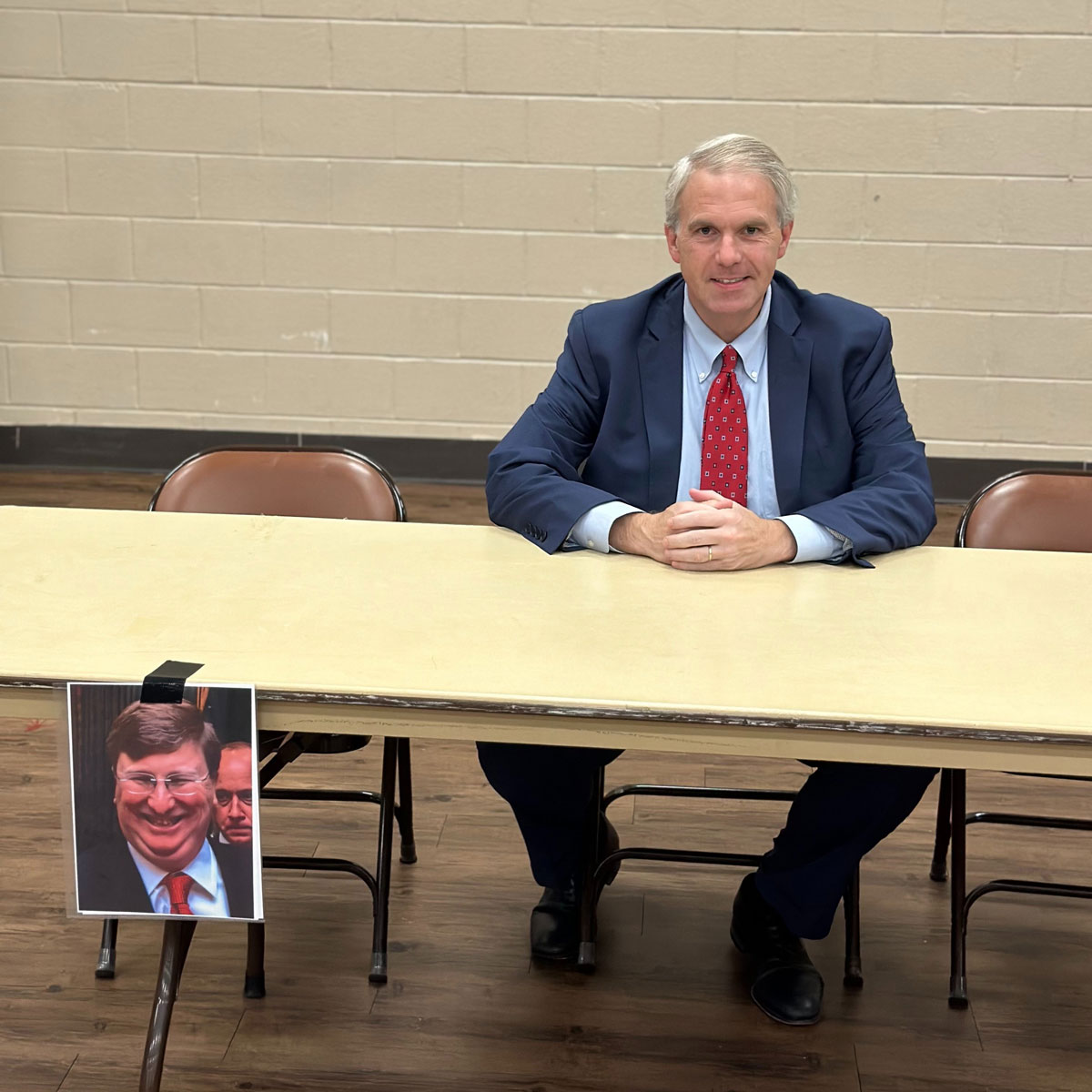 Brandon Presley sits at an empty table with a photo of Tate Reeves taped to the front