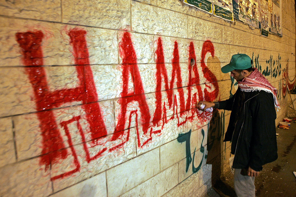 A man in a cap paints the word Hamas in large letters on a wall