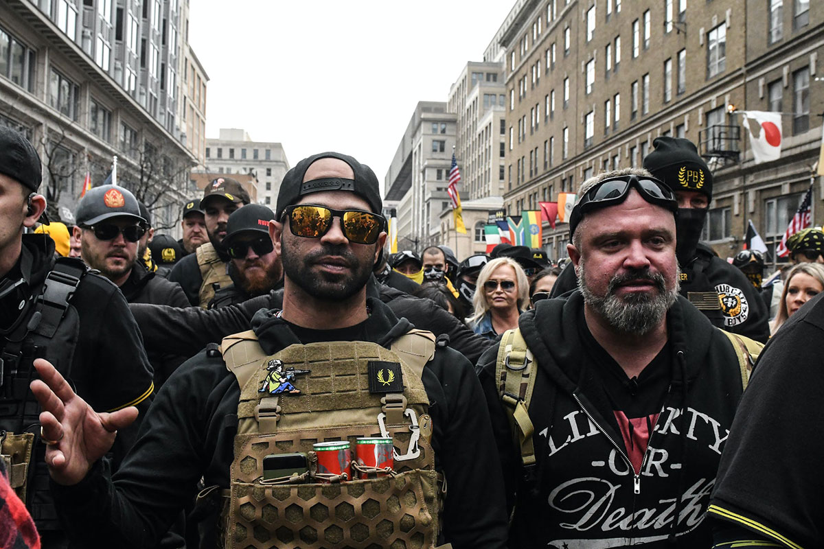 Focus on two men in a large street crowd of people dressed in black and quasi-military attire