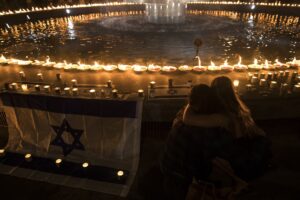 Two people hug and look on to a fountain surrounded by lit candles of rememberance