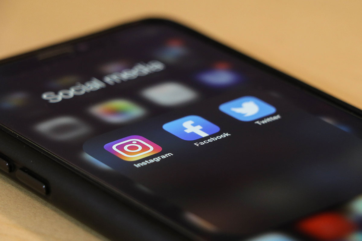 A cell phone's social media folder visible on the screen. Instagram, Facebook, and Twitter icons are clearly visible