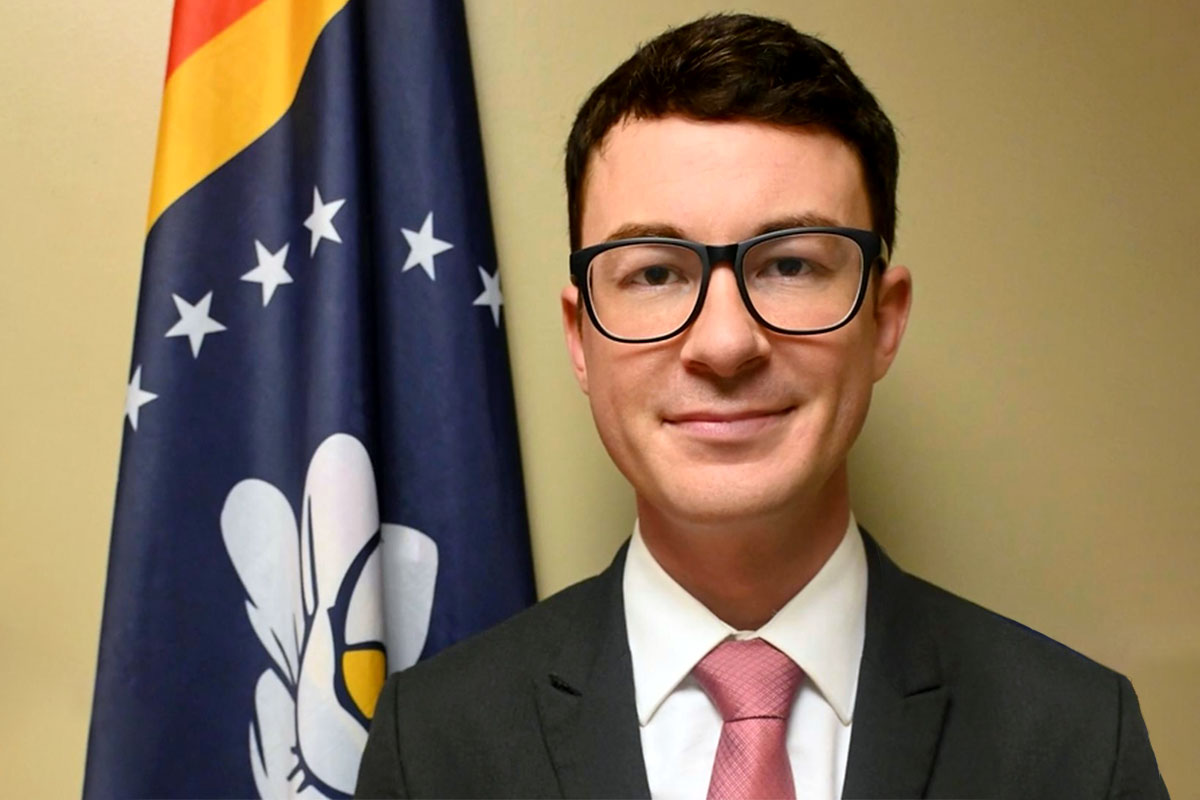 Headshot of D. Ryan Grover standing before the Mississippi state flag