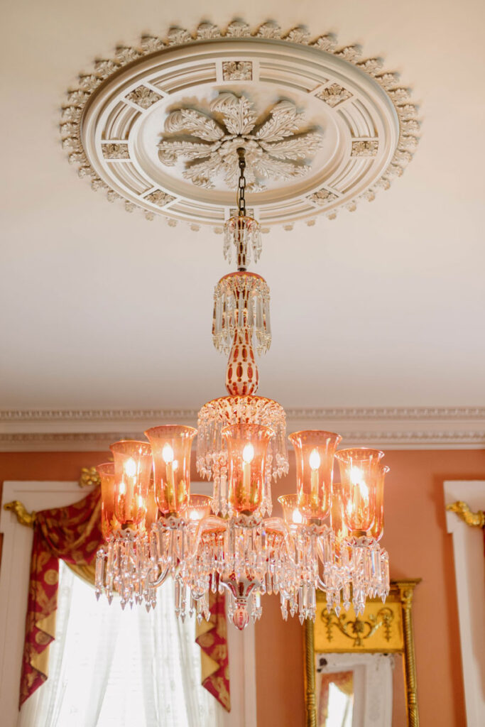 a photo of a glowing pink chandelier hanging from an ornate ceiling with crystals hanging beneath its lamps