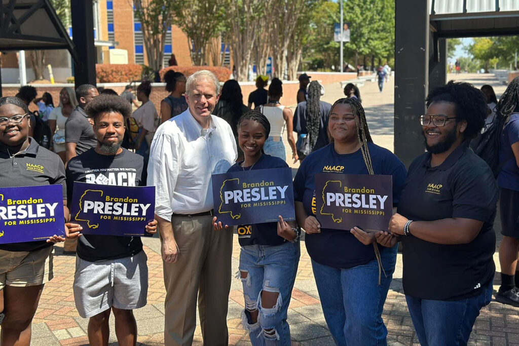 Brandon Presley stands with potential voters holding his campaign signs at JSU
