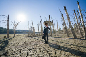 A man in suit holds up an umbrella while standing in a dry cracked land area