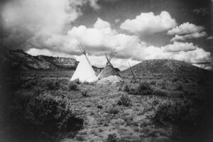 Teo tipi are set up on flat scrub land, hills visible in the background (land acknowledgement)