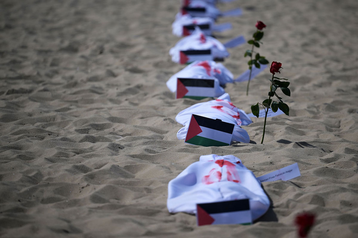 white blankets with red paint on them lie next to Palestinian flags on a beach (Gaza)