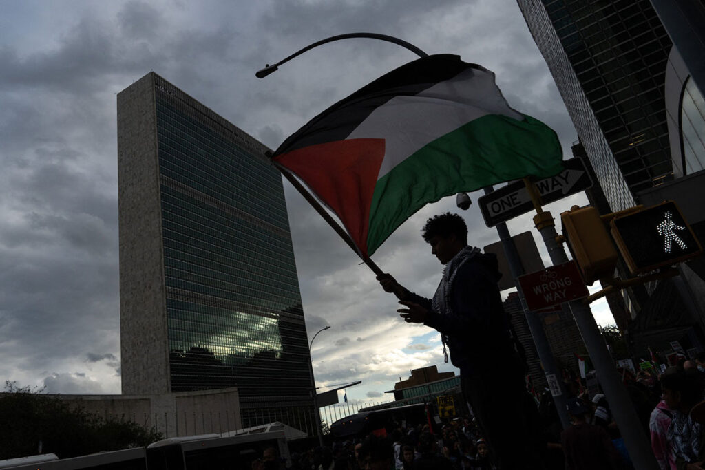 A person holds a Palestine flag aloft neat the United Nations building
