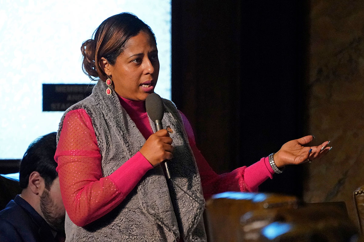 Zakiya Summers speaks under a spotlight to a group