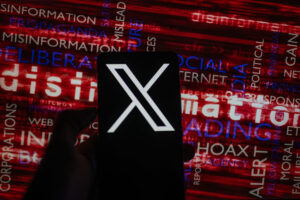 A darkened hand holds a cell phone up with a giant "X" logo on the screen, in front of a red word cloud of Misinformation (Israel-Hamas War)